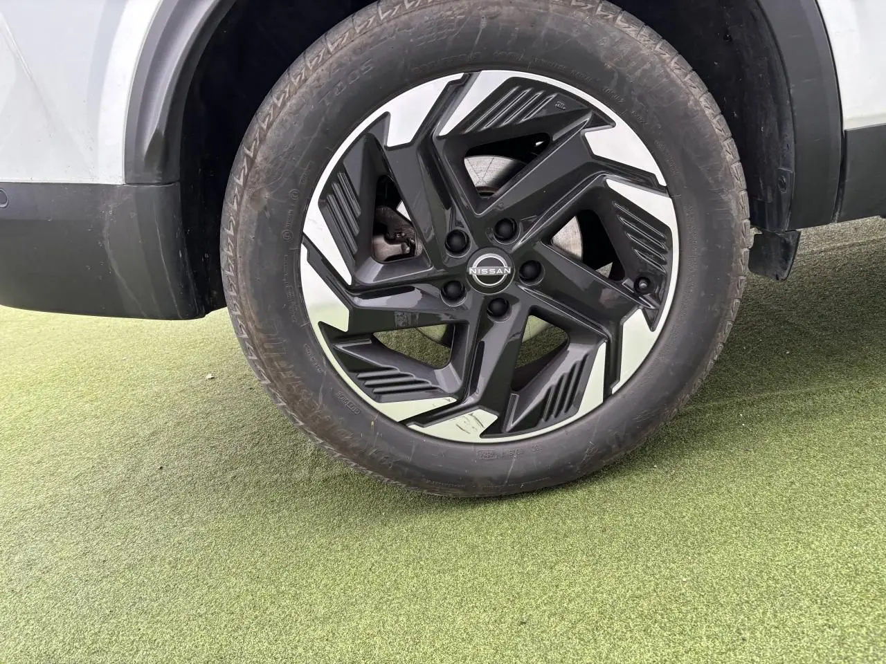 Gros plan sur la roue avant droite du Nissan Qashqai blanc nacré, jante alliage 18 pouces noire et argentée.