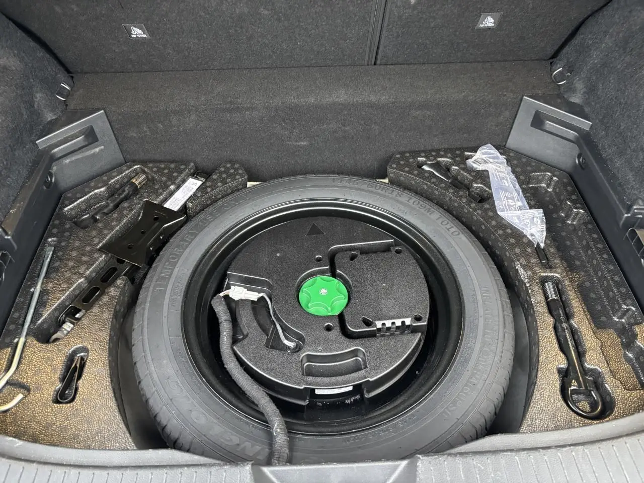 Vue plongeante sur la roue de secours temporaire noire dans le coffre du Nissan Qashqai blanc nacré 2025.