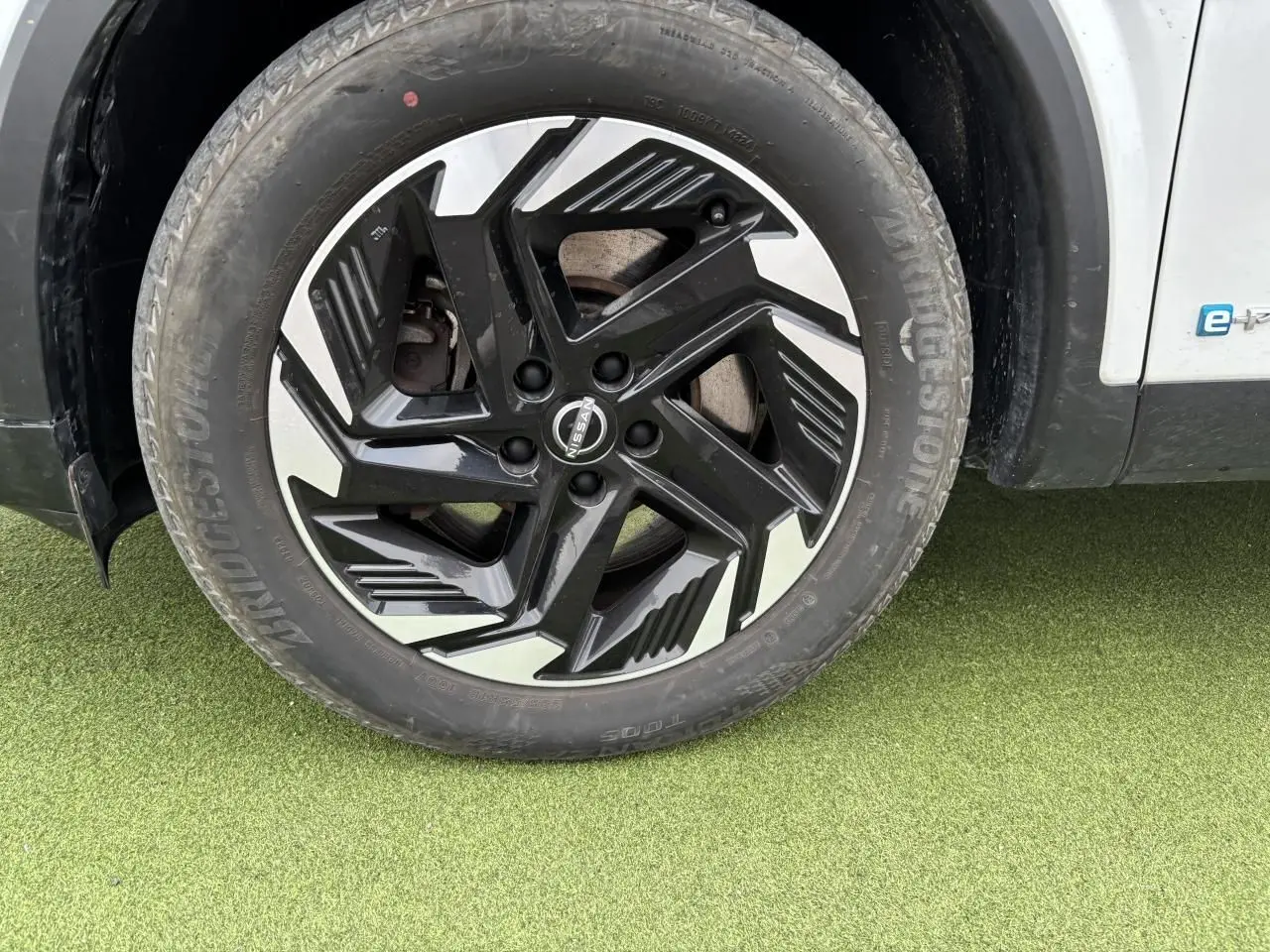 Gros plan sur la roue avant gauche du Nissan Qashqai blanc nacré, avec jante alliage noire et argentée au design moderne.