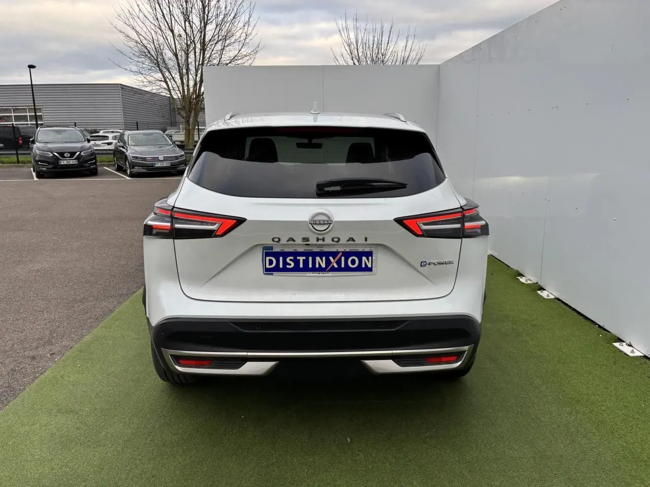 Vue arrière d'un Nissan Qashqai blanc nacré avec feux LED et logo E-POWER sur un sol vert artificiel.