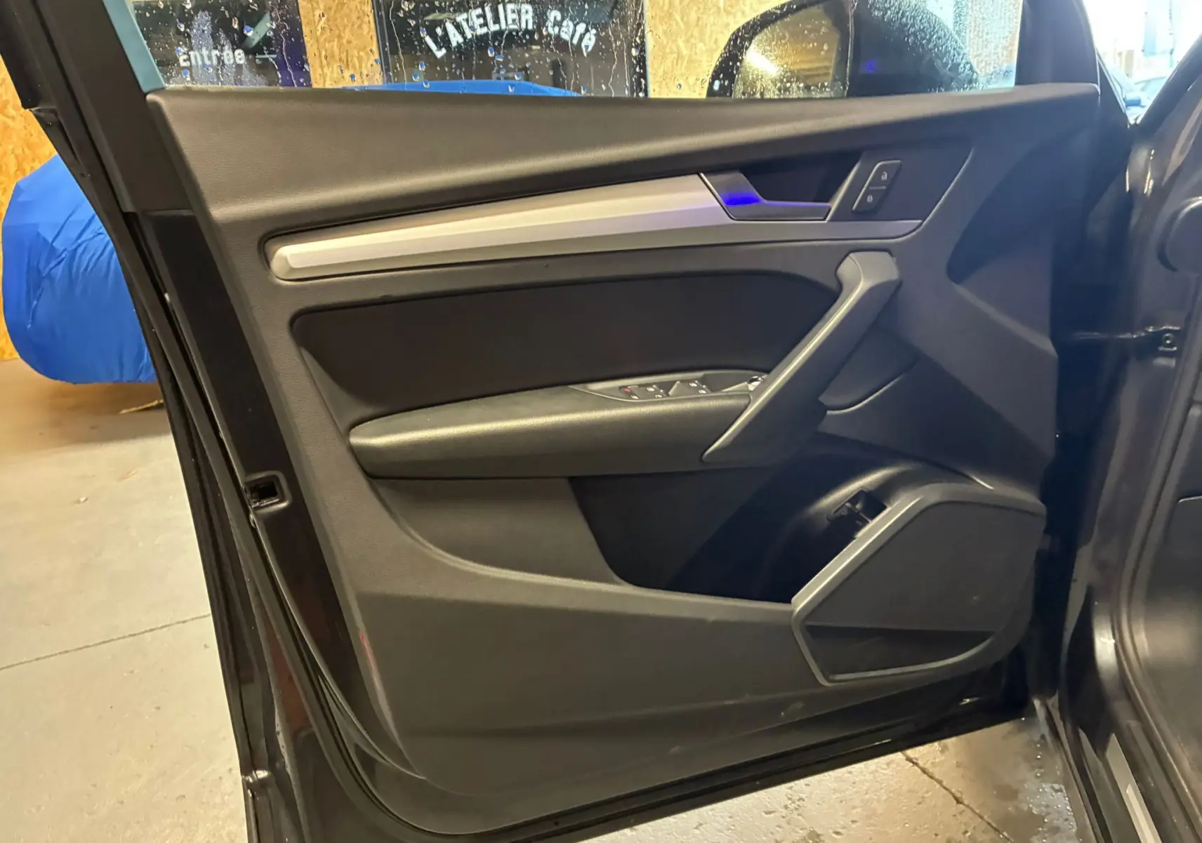 Vue intérieure de la porte avant gauche gris foncé de l'Audi Q5 2024 avec insert argent et commandes électriques.