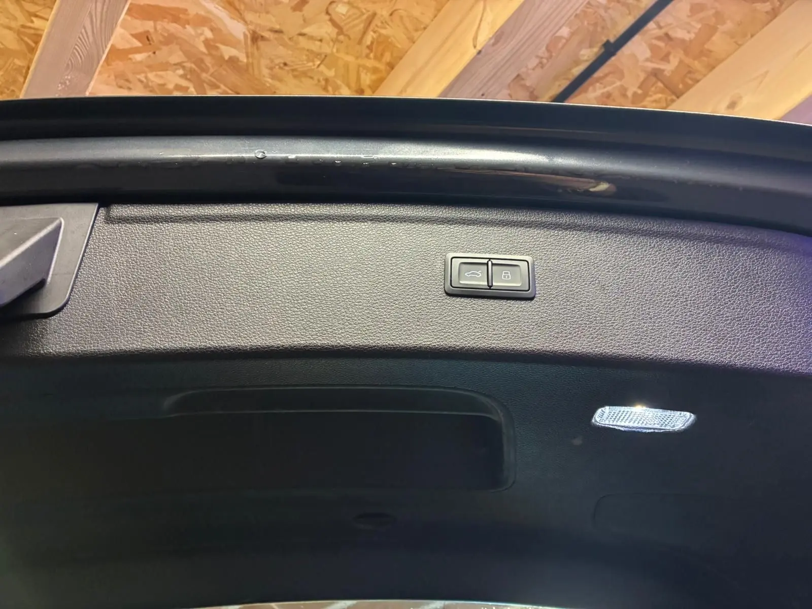 Bouton d'ouverture et de verrouillage sur le hayon intérieur noir du coffre d'un Audi Q5 gris 2024.
