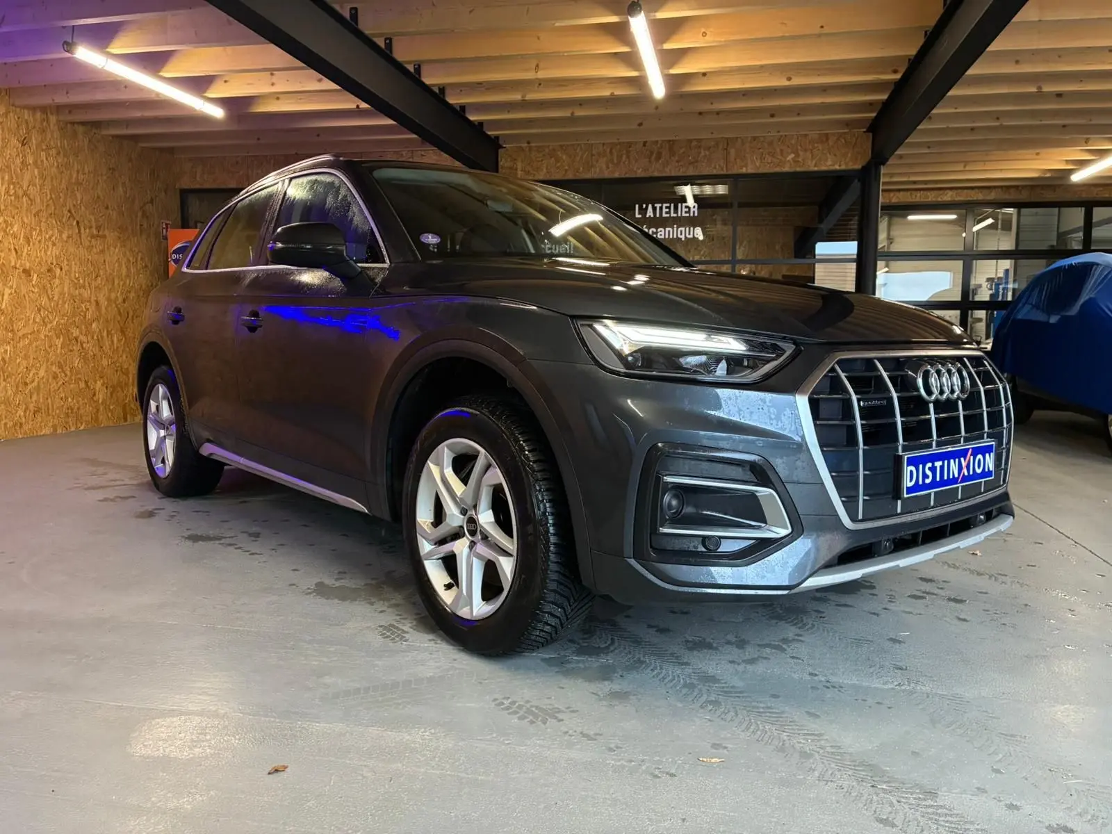 Audi Q5 gris hybride rechargeable vu en 3/4 avant droit dans un garage avec jantes 5 branches doubles.