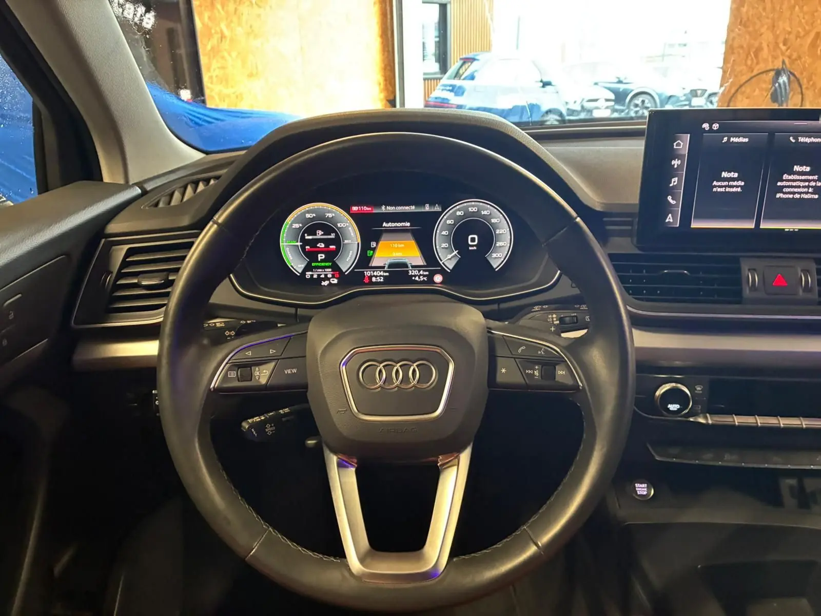 Vue intérieure centrée sur le volant cuir noir et le tableau de bord digital de l'Audi Q5 hybride rechargeable 2024.