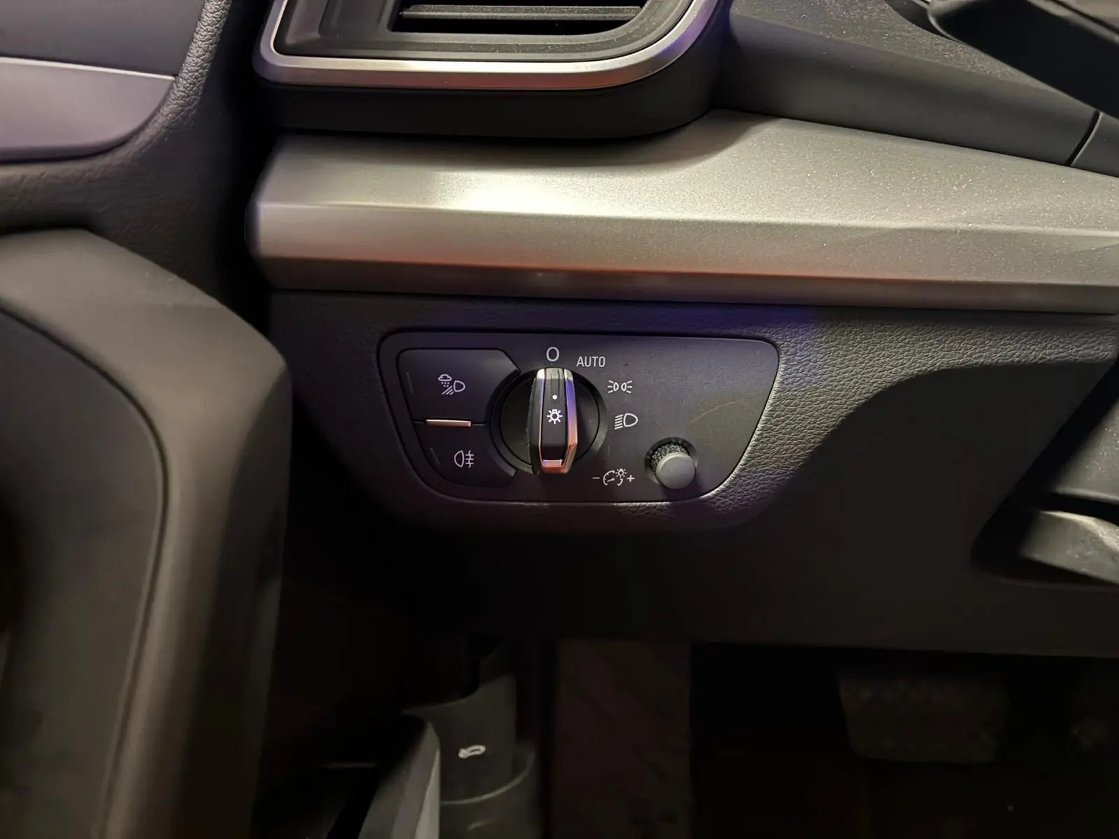 Gros plan sur le panneau de commande des phares à gauche du tableau de bord d’un Audi Q5 gris 2024.