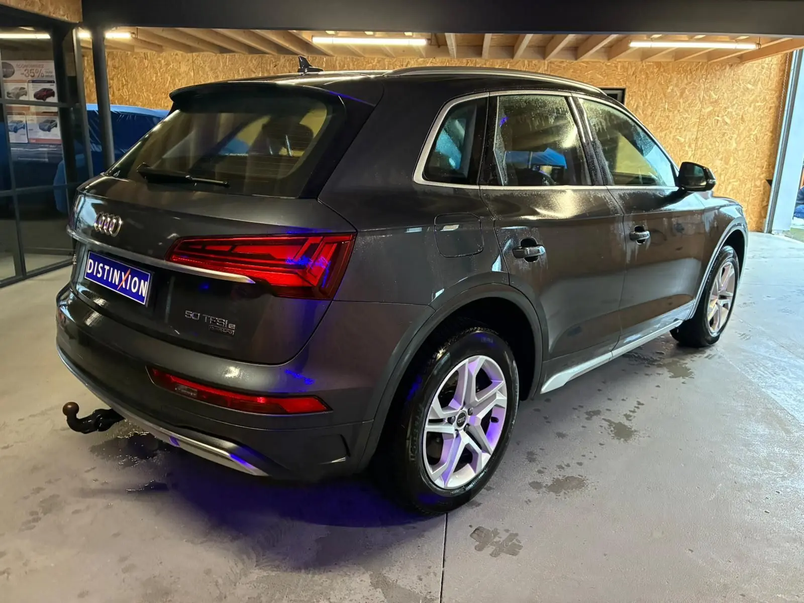 Audi Q5 gris en vue 3/4 arrière droit, avec jantes 5 branches doubles et crochet d'attelage visible.