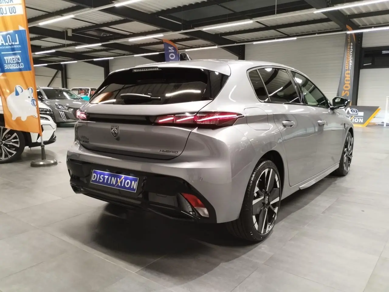 Vue 3/4 arrière droite d'une Peugeot 308 hybride gris Artense avec feux arrière LED en forme de griffes et jantes alliage 18 pouces.