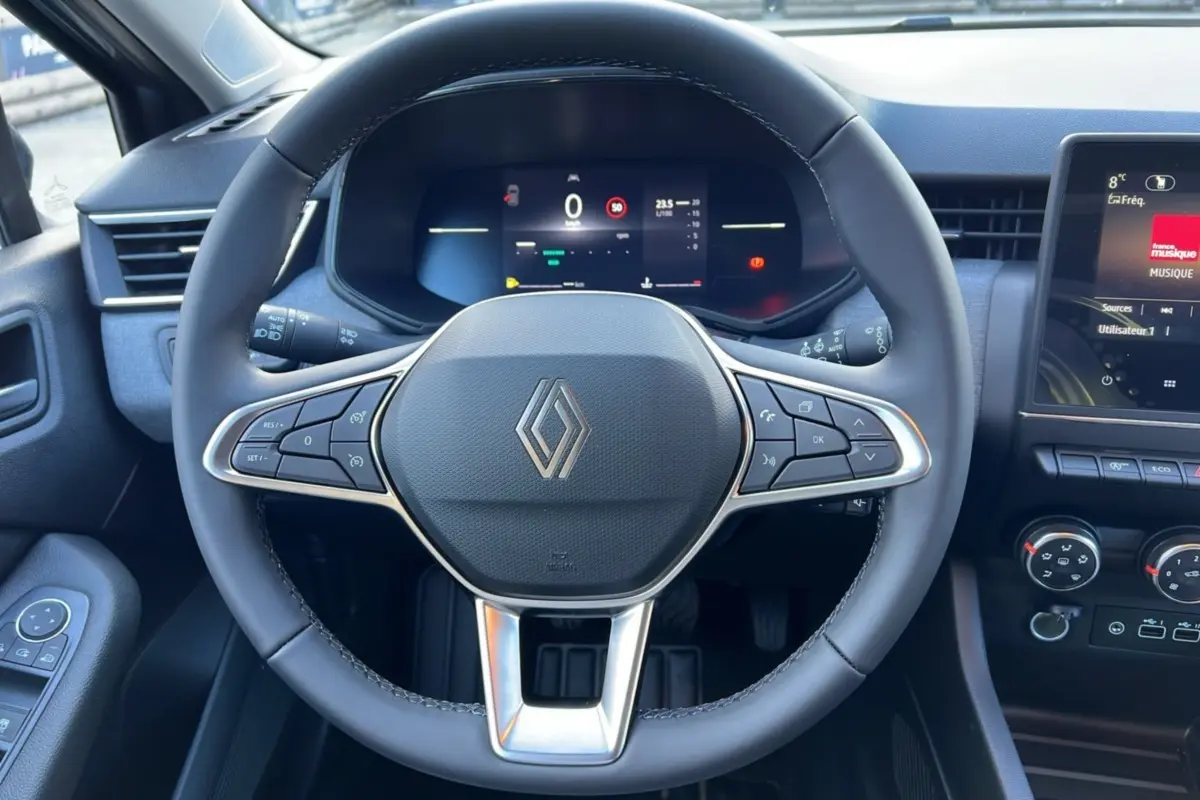 Vue intérieure centrée sur le volant multifonctions noir de la Renault Clio 2025 avec tableau de bord digital et écran tactile.
