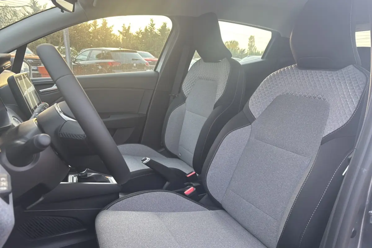 Vue intérieure côté conducteur de la Renault Clio gris schiste, mettant en valeur les sièges avant en tissu bicolore.