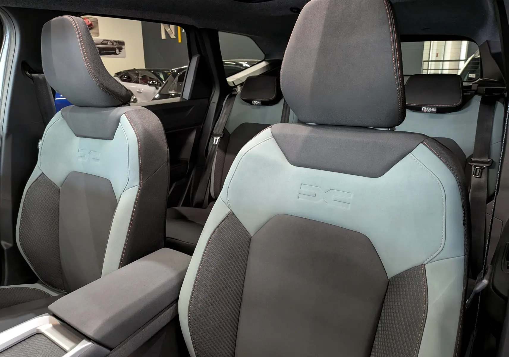 Vue intérieure rapprochée des sièges avant gris clair et noir du Dacia Bigster Hybrid-G 150 4x4, avec surpiqûres orange.