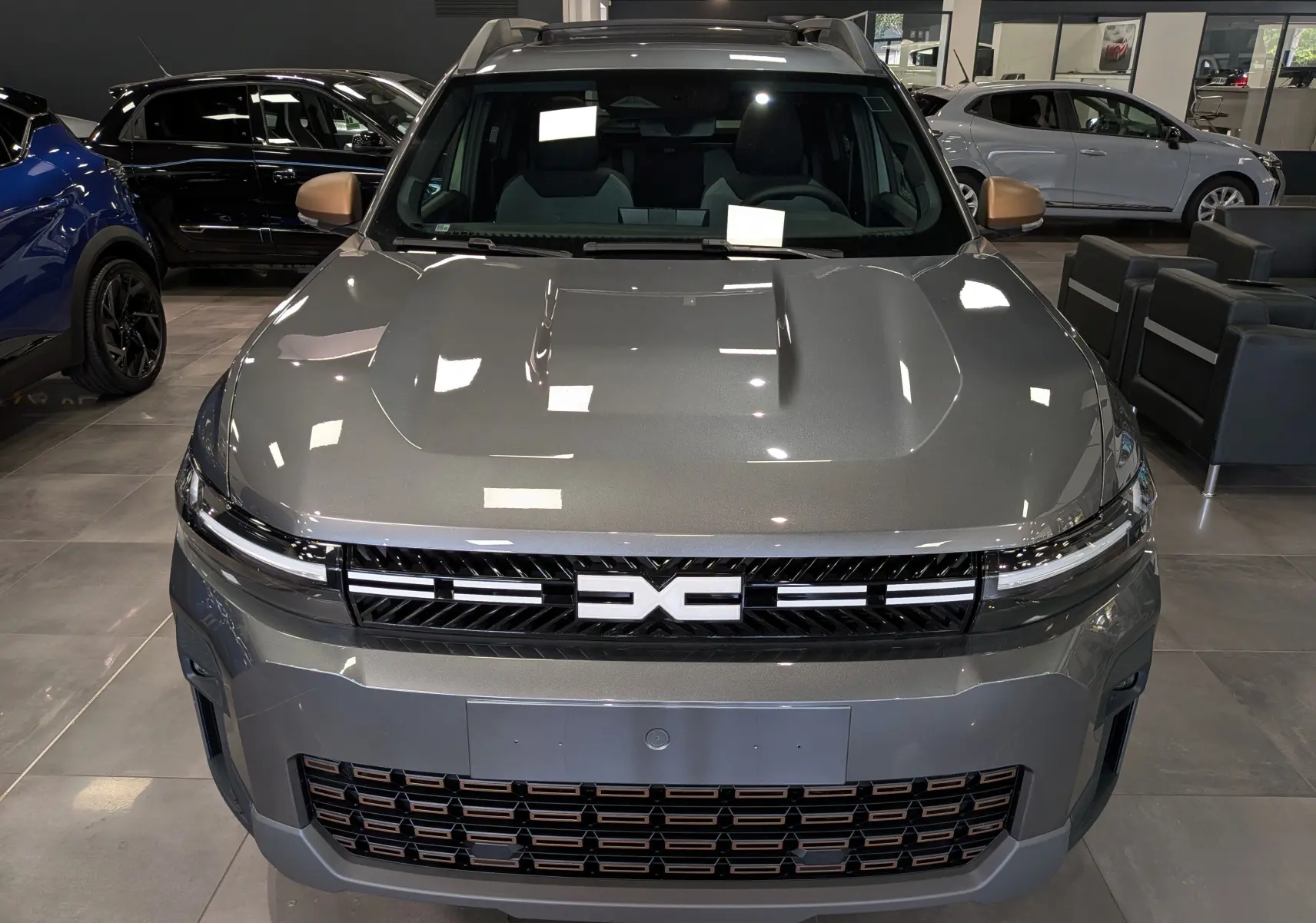 Vue frontale du Dacia Bigster Hybrid-G 150 4x4 en gris schiste avec calandre noire et détails cuivrés en showroom.