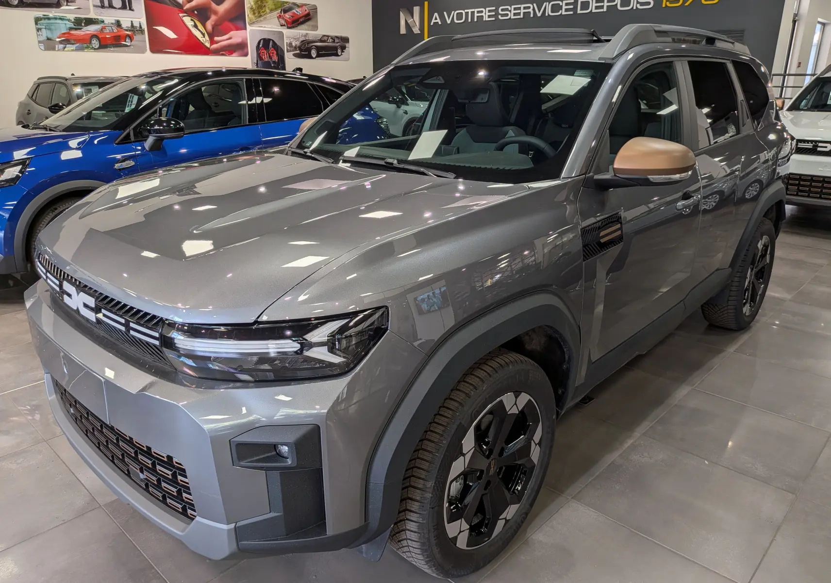 Vue 3/4 avant droit du Dacia Bigster Hybrid-G 150 4x4 gris schiste avec rétroviseurs couleur bronze en showroom.