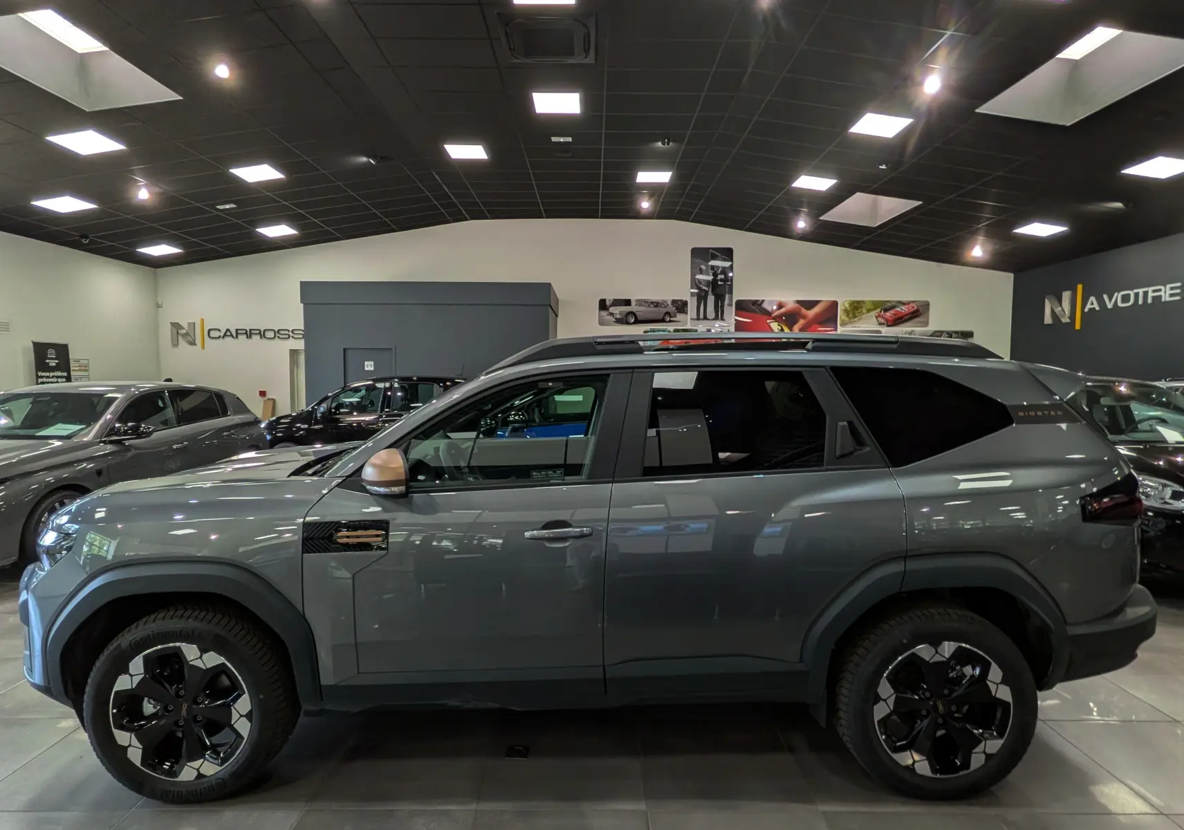 Vue de profil côté gauche du Dacia Bigster Hybrid-G 150 4x4 gris schiste avec jantes bi-ton et rétroviseurs bronze.
