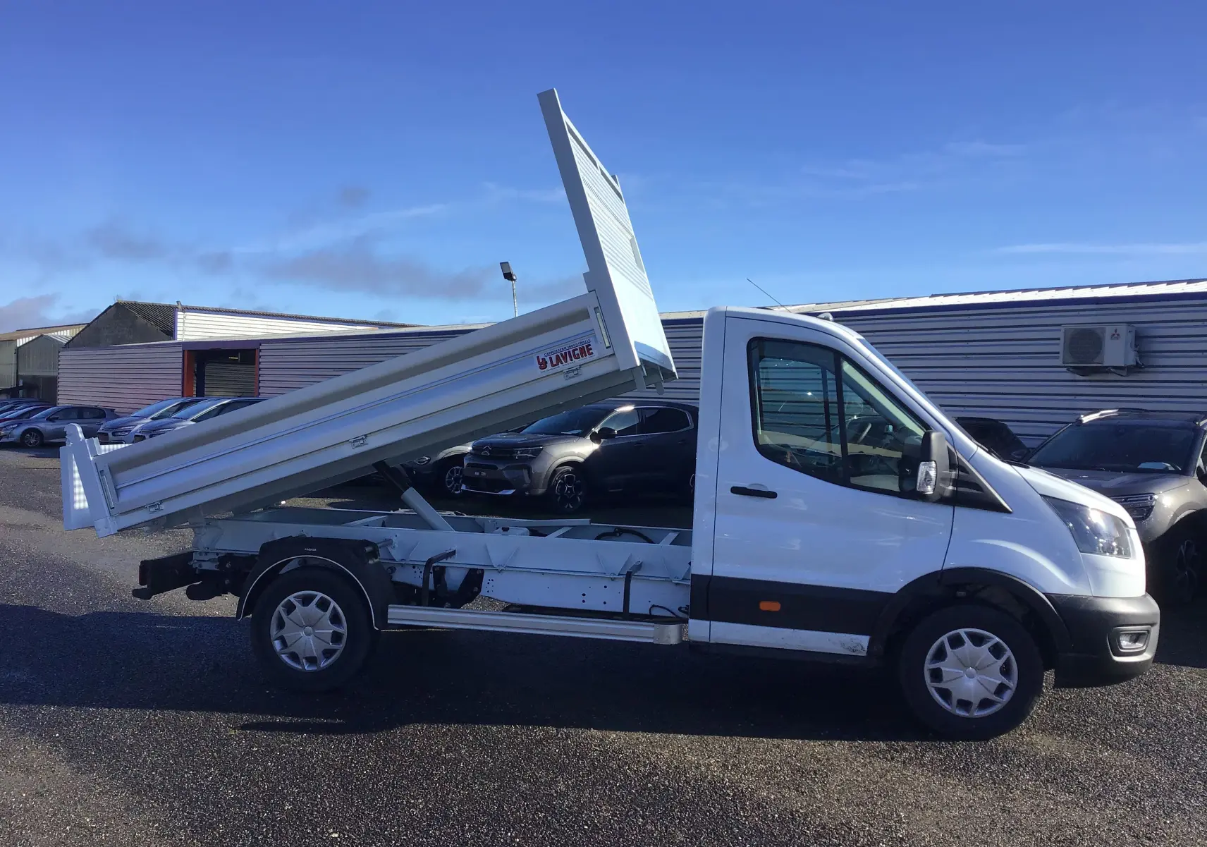 Ford Transit Chassis cabine blanc vu de profil côté gauche, avec benne basculante levée et marquage Lavigne visible.