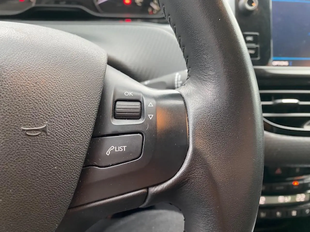 Gros plan sur le volant noir du Peugeot 2008 2018 avec commandes intégrées et écran tactile en arrière-plan.