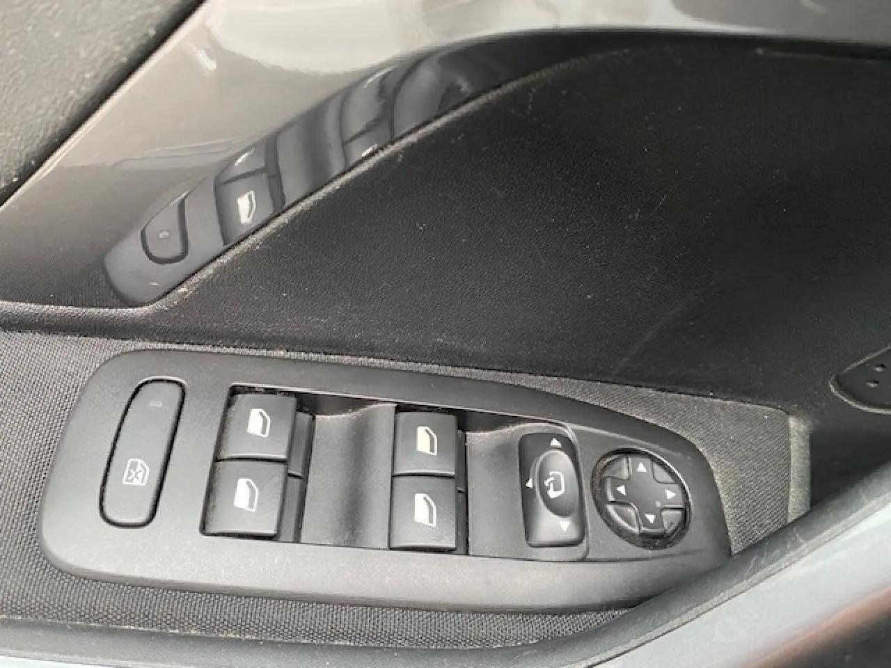 Gros plan sur les commandes des vitres et rétroviseurs côté gauche intérieur d'une Peugeot 2008 blanche de 2018.