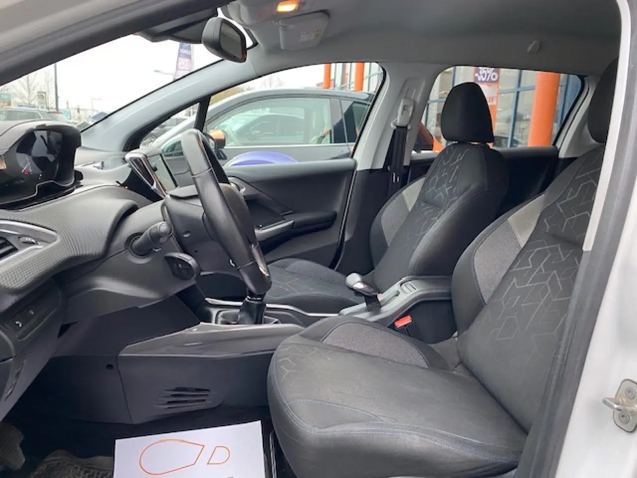 Intérieur avant du Peugeot 2008 blanc, montrant les sièges tissu noir et gris et le tableau de bord moderne côté conducteur.