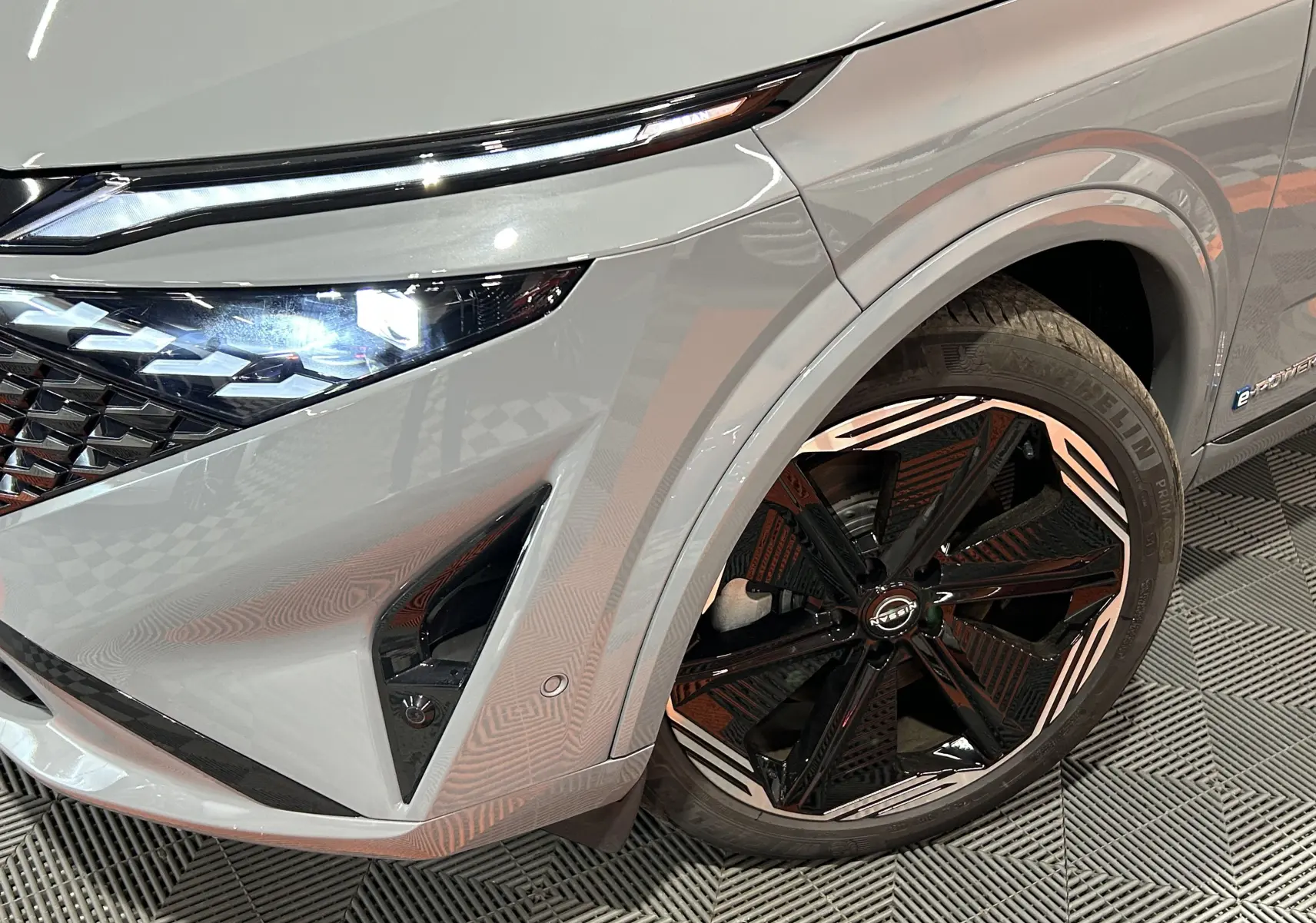 Gros plan sur l'avant droit du Nissan Qashqai gris céramique avec jante noire et blanche et phare LED allumé.