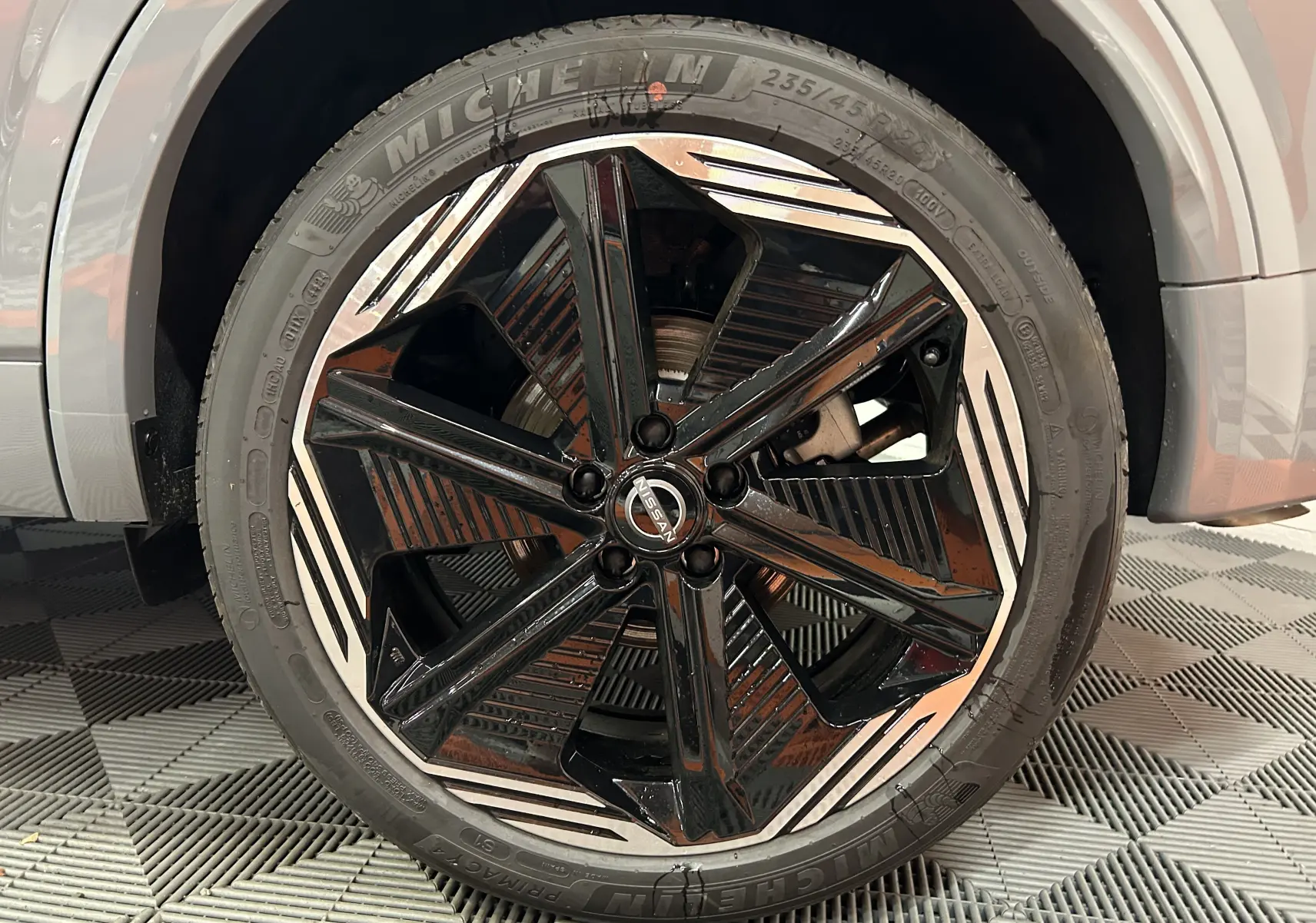 Gros plan sur la jante noire et argentée du Nissan Qashqai 2025, avec pneu Michelin et partie de la carrosserie gris céramique visible.