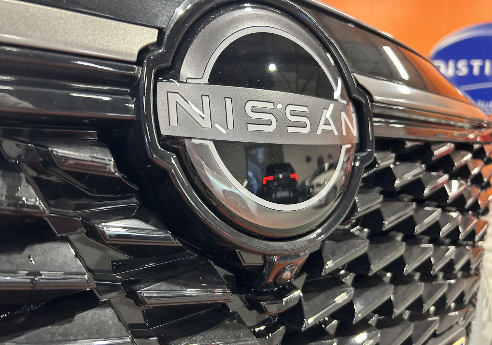 Gros plan sur la calandre noire brillante du Nissan Qashqai 2025 avec logo central et caméra frontale intégrée.