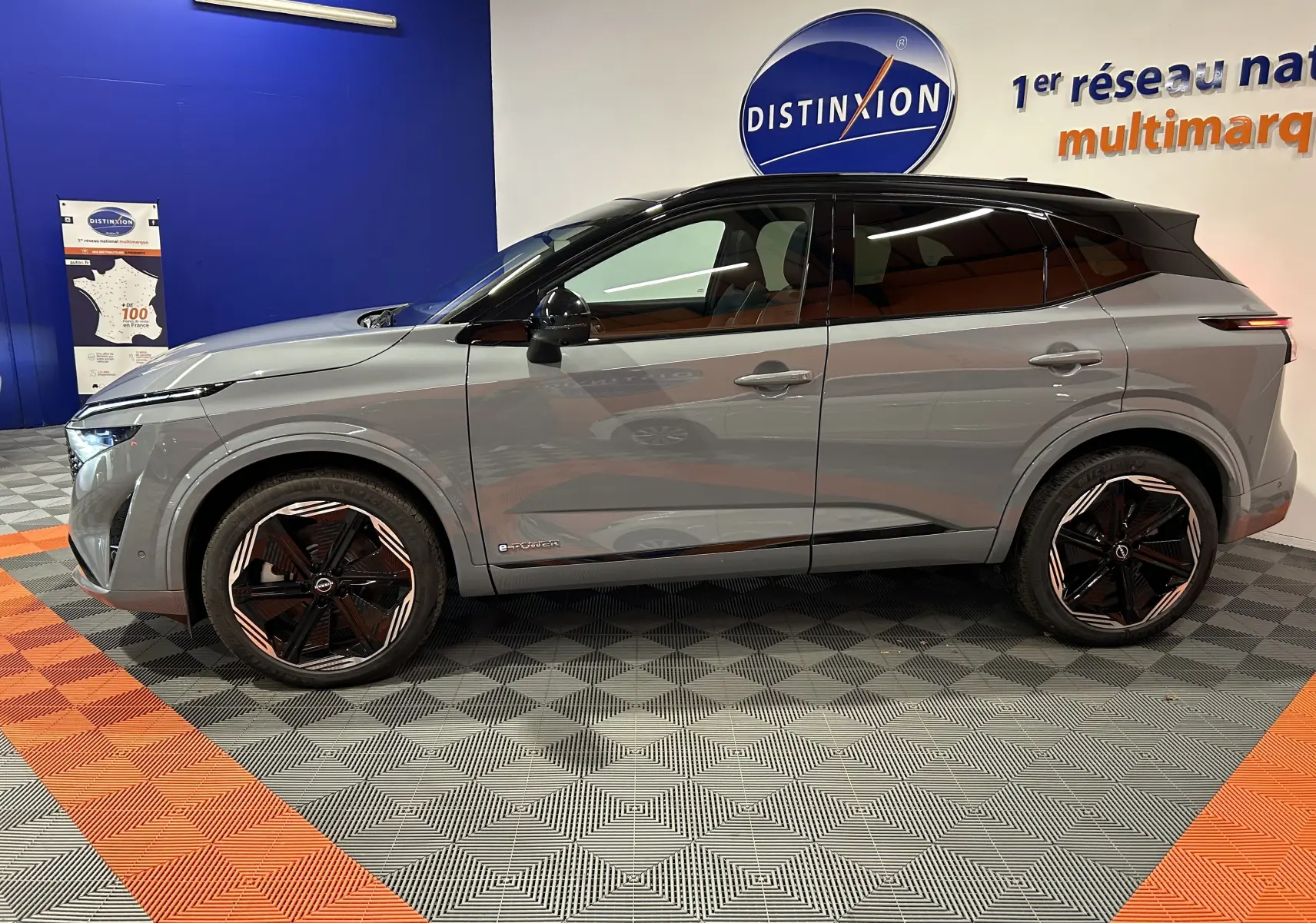 Profil côté gauche du Nissan Qashqai 2025 gris céramique avec toit noir et jantes noires stylisées en intérieur showroom.