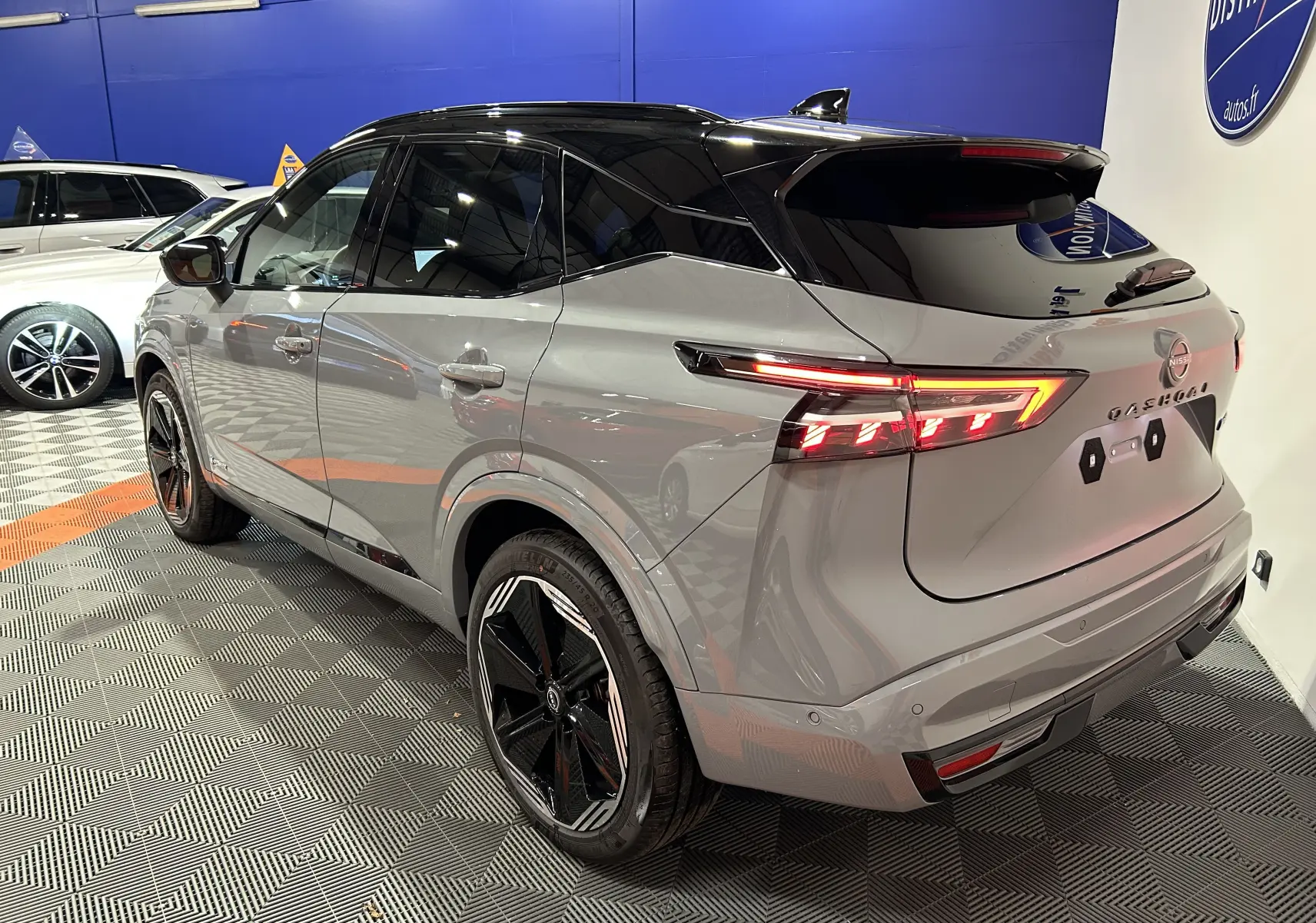Vue 3/4 arrière droite du Nissan Qashqai gris céramique avec toit noir et feux arrière LED allumés.