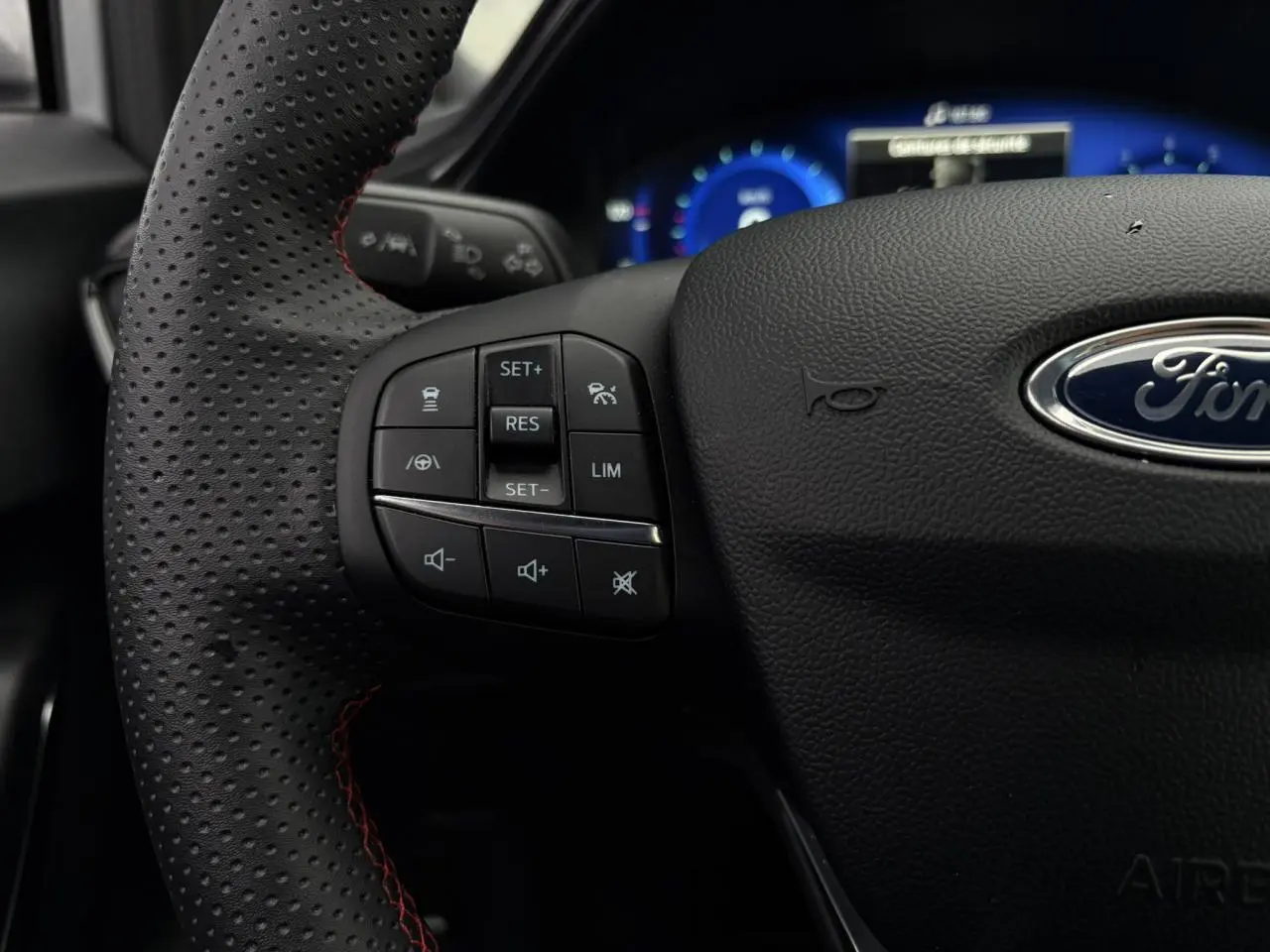Gros plan sur le volant ST-Line perforé noir avec surpiqûres rouges et commandes multifonctions du Ford Puma 2023.