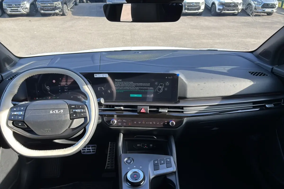 Vue intérieure frontale du tableau de bord du Kia Sportage blanc nacré, avec écran tactile large et volant multifonctions.
