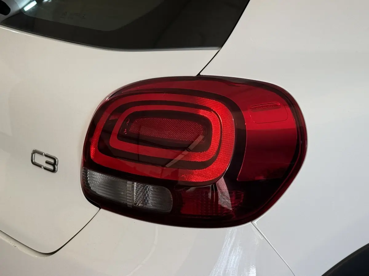 Gros plan sur le feu arrière droit rouge et blanc d'une Citroën C3 blanche, avec logo C3 visible sur la carrosserie.