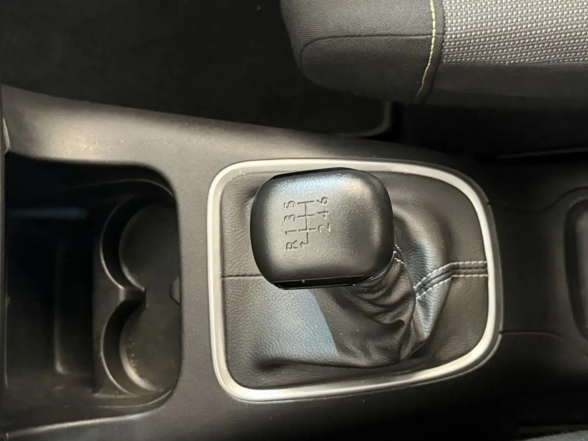 Gros plan sur le levier de vitesse manuel noir de la Citroën C3 blanche, entouré de garniture grise et console noire.