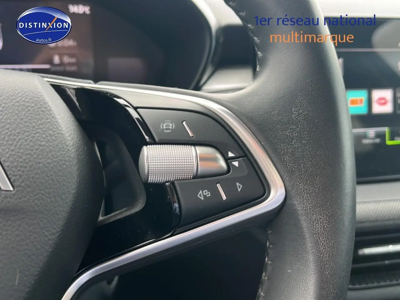 Gros plan sur les commandes gauche du volant cuir multifonction d'une Skoda Fabia bleue, avec écran tactile en arrière-plan.
