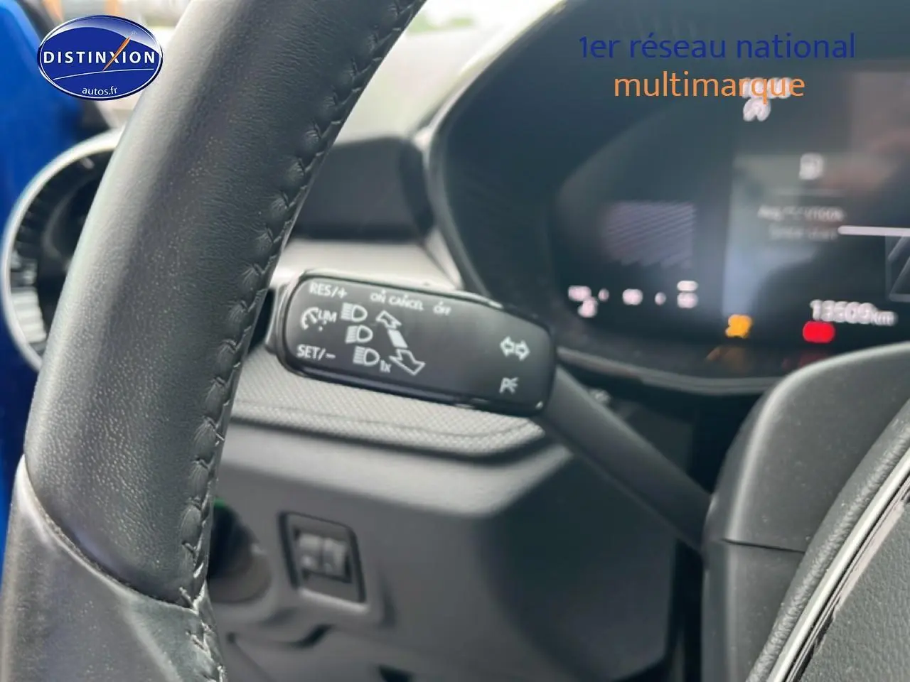 Gros plan sur le volant cuir et la commande multifonction noire dans l'habitacle sombre d'une Skoda Fabia bleue.