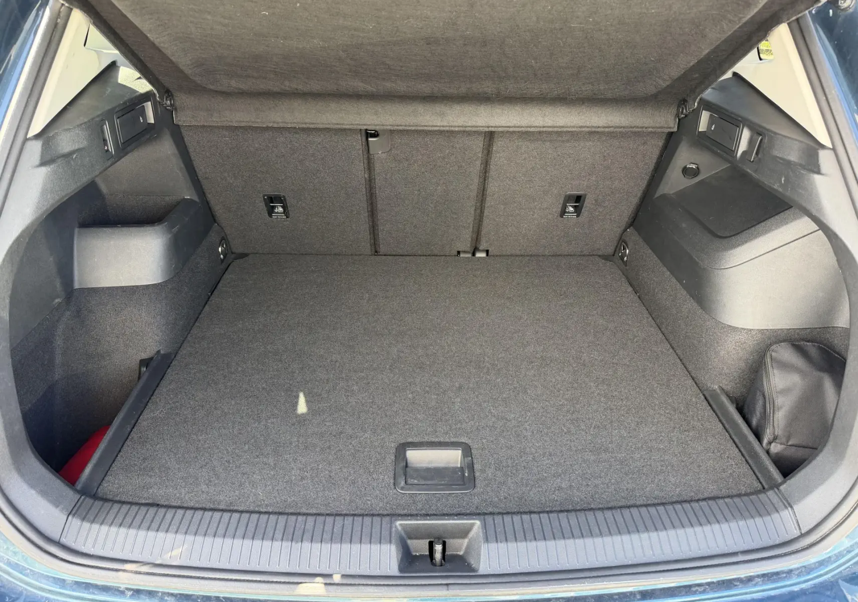 Coffre ouvert vu de l'arrière d'un Volkswagen Tiguan bleu 2025, avec plancher plat et habillage gris foncé.