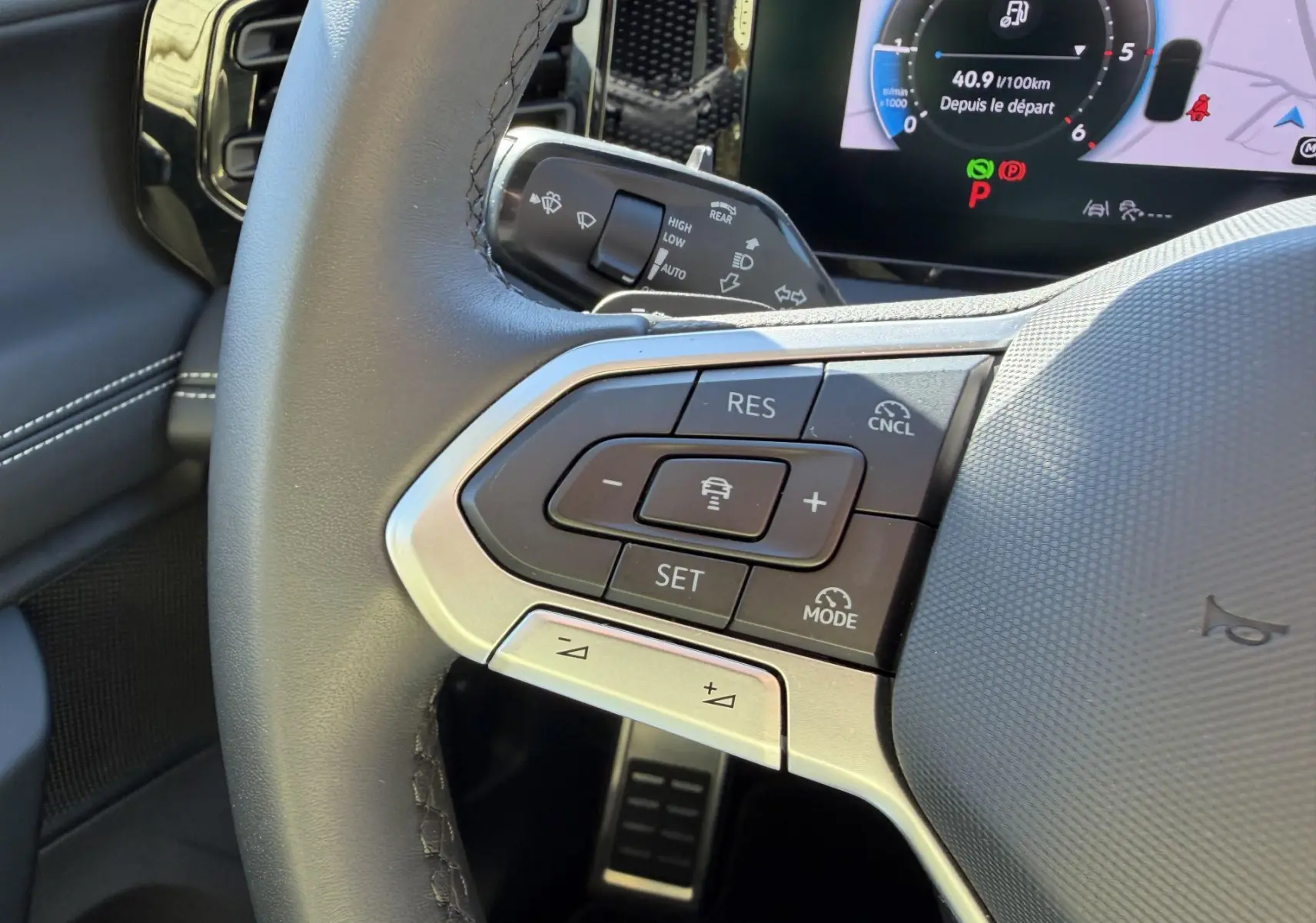 Gros plan sur le volant multifonction cuir du Volkswagen Tiguan 2025, avec commandes de régulateur de vitesse et tableau de bord numérique en arrière-plan.