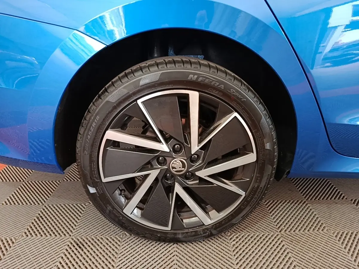 Gros plan sur la roue arrière droite d’une Skoda Octavia bleu avec jante alliage noire et argentée.