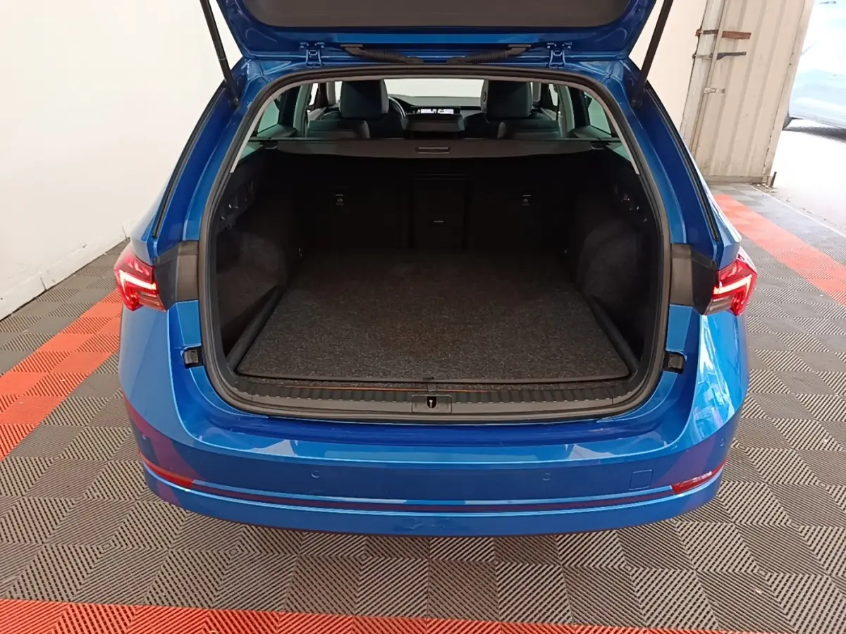 Vue arrière d'un Skoda Octavia bleu 2022 avec coffre ouvert montrant un espace de chargement spacieux et tapis gris.