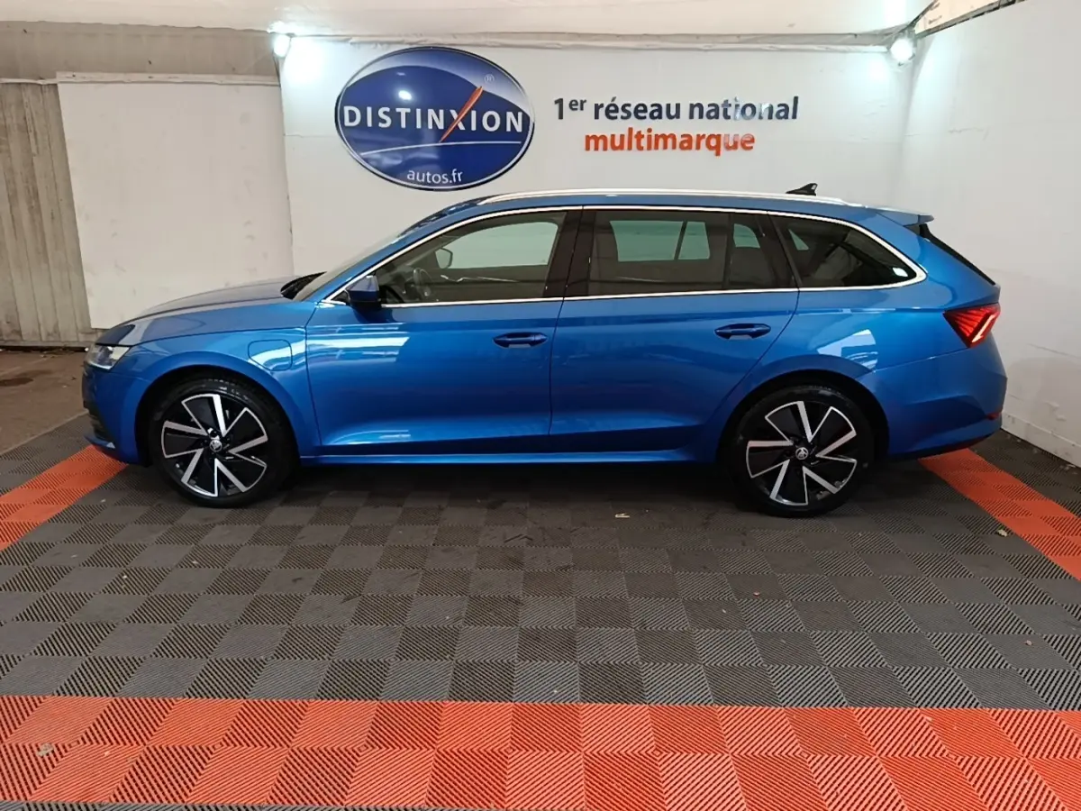 Vue de profil côté gauche d'une Skoda Octavia break bleu 2022 hybride rechargeable, jantes alliage noires et argent.