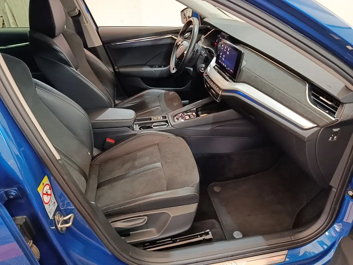 Vue intérieure côté conducteur d'une Skoda Octavia bleu 2022, avec sièges en cuir noir et tableau de bord digital.