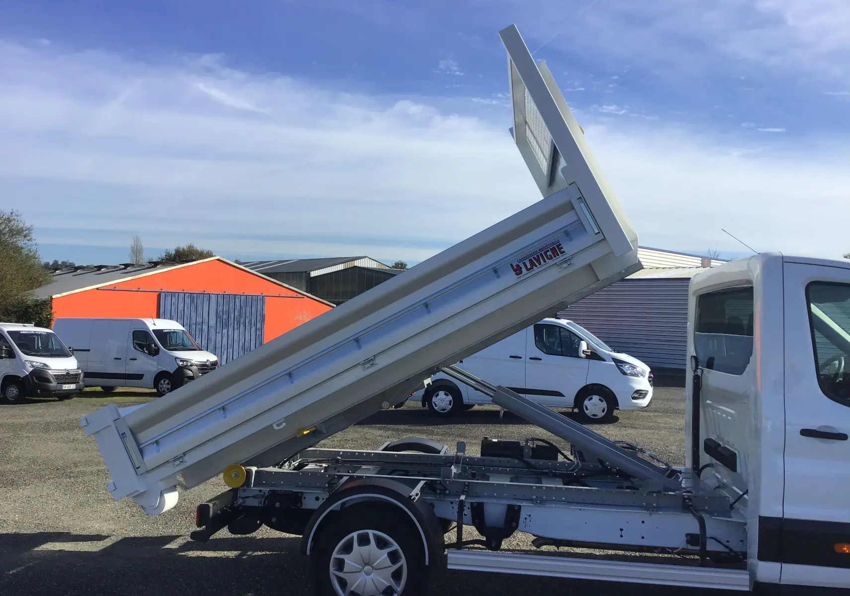 Vue de profil côté gauche d'un Ford Transit blanc avec benne relevée et bras polybenne visible en extérieur.
