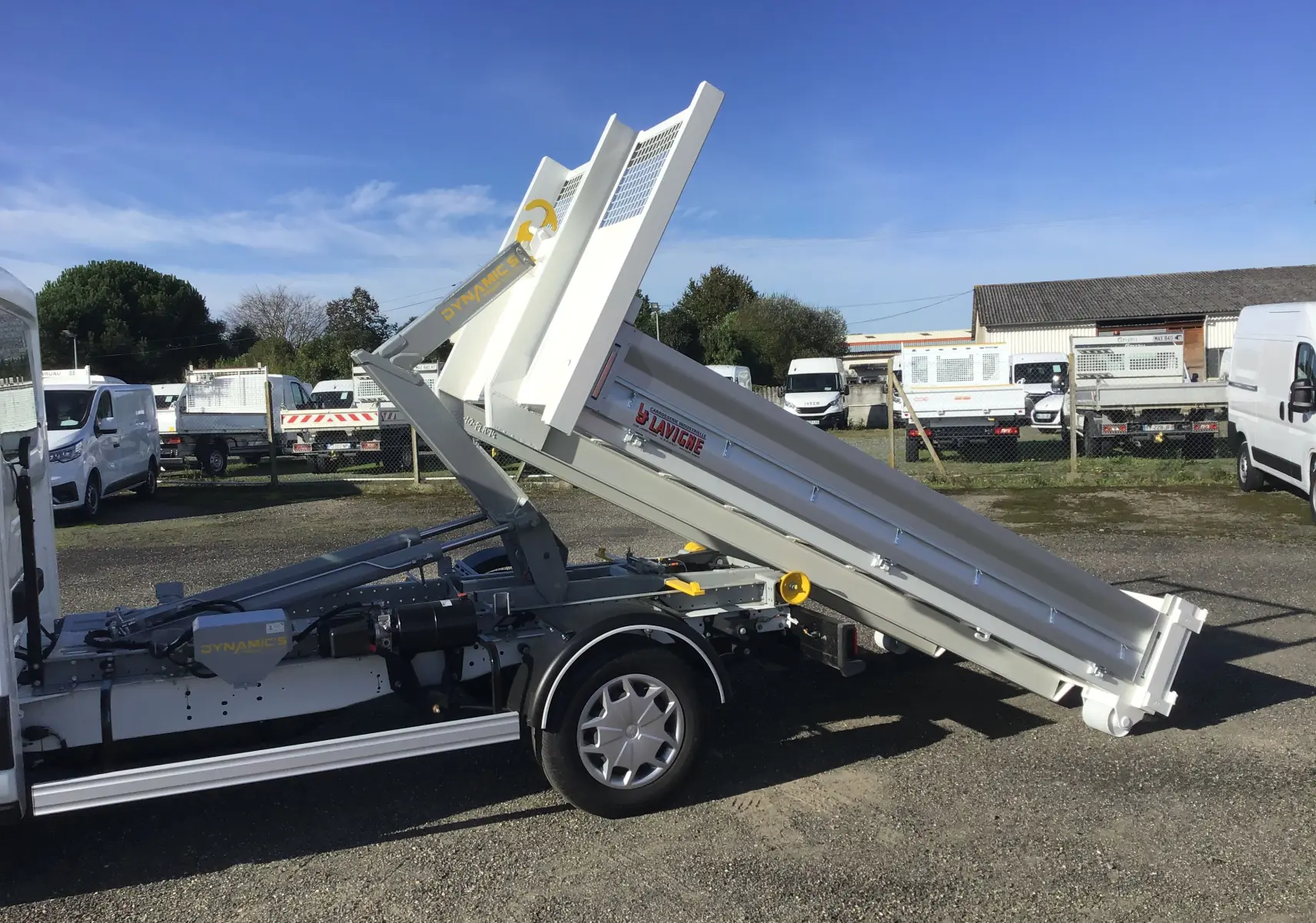 Vue latérale droite d'un Ford Transit blanc avec benne basculante relevée et bras polybenne visible en extérieur.