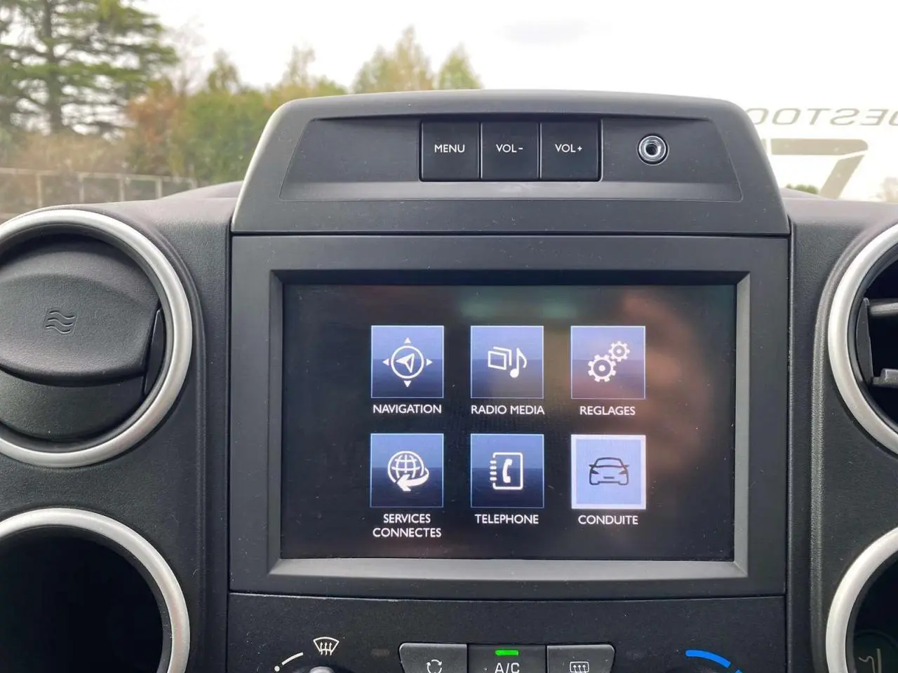 Écran tactile multifonctions allumé au centre du tableau de bord du Peugeot Partner gris, entouré de bouches d'aération rondes.