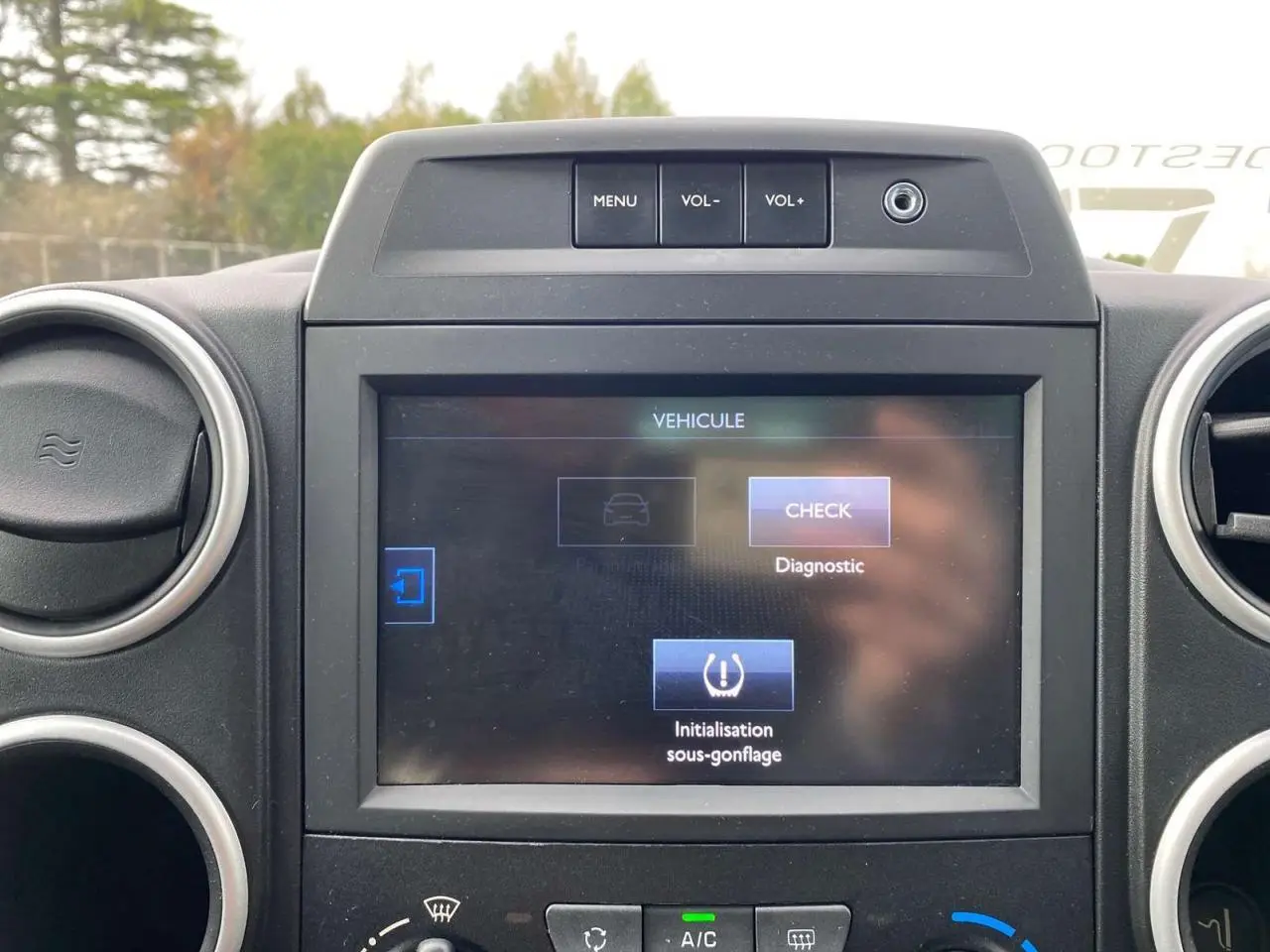 Écran tactile multifonctions allumé au tableau de bord du Peugeot Partner gris, avec commandes de volume visibles.