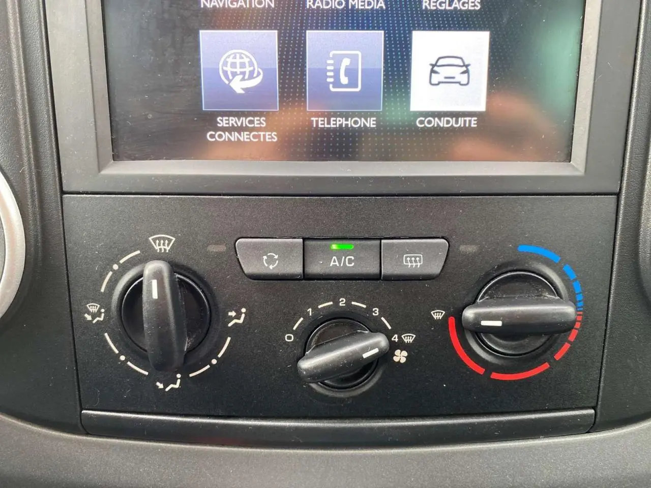Gros plan sur la console centrale du Peugeot Partner gris, montrant les commandes de climatisation et l'écran tactile multifonctions.