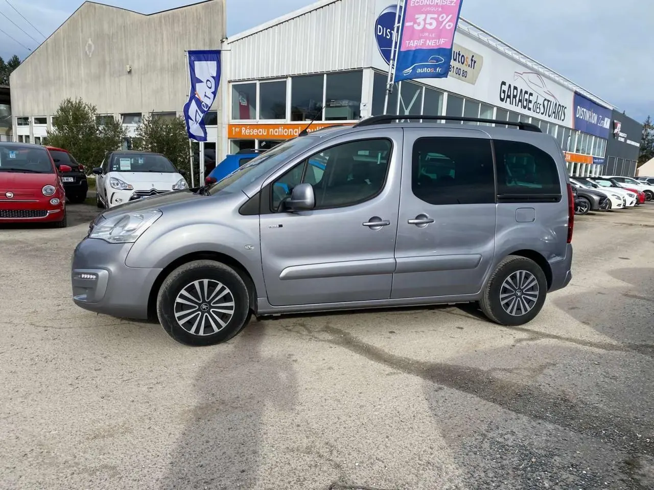 Profil côté gauche d'un Peugeot Partner gris Artense 2017 avec portes coulissantes et vitres teintées, stationné en extérieur.