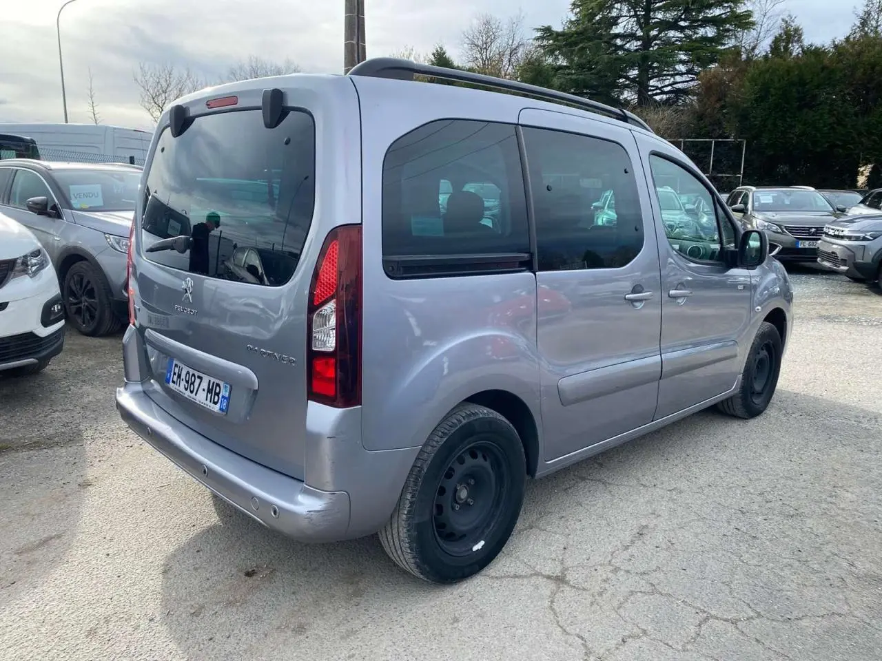 Vue 3/4 arrière droite d'un Peugeot Partner gris Artense avec porte latérale coulissante et roue de secours noire.