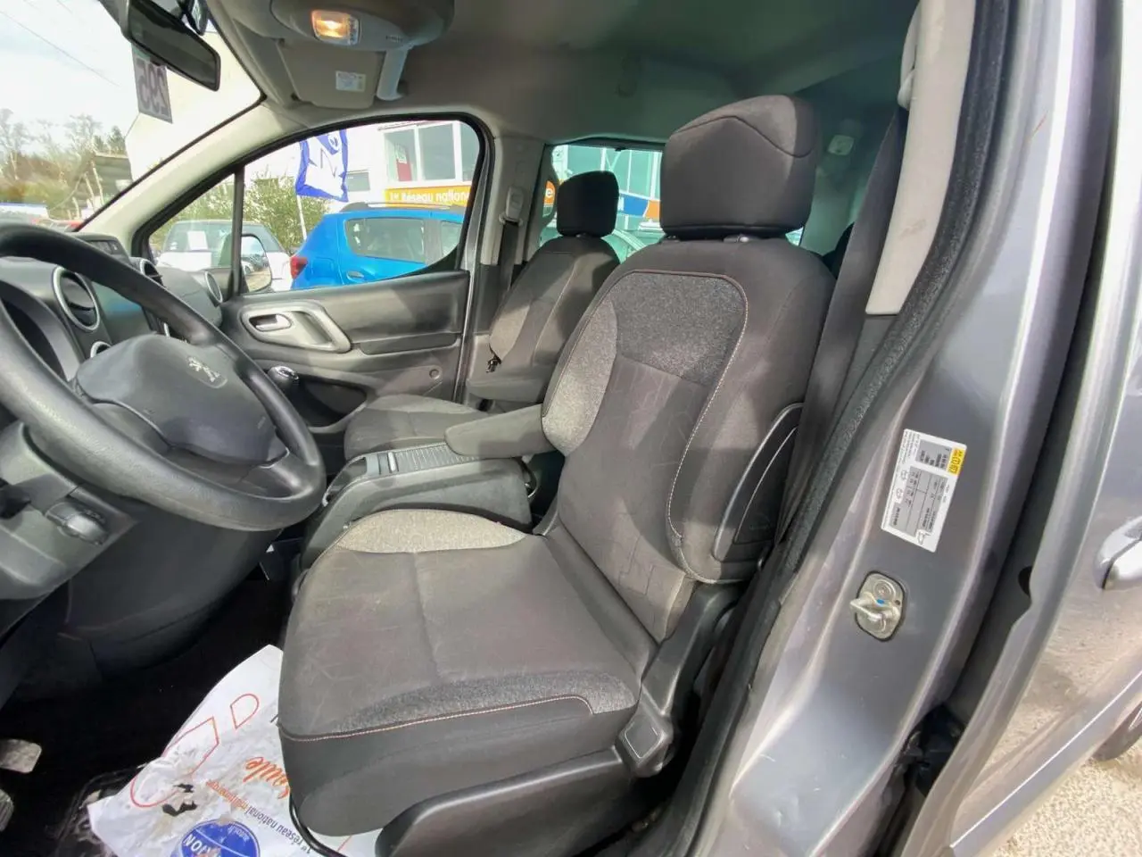 Vue intérieure côté conducteur du Peugeot Partner gris Artense de 2017, montrant les sièges et le volant.