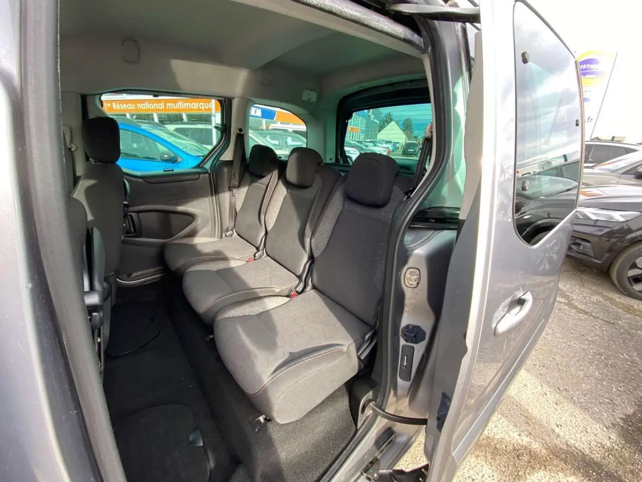 Vue intérieure côté droit du Peugeot Partner gris Artense, montrant la banquette arrière 2/3-1/3 et la porte coulissante ouverte.