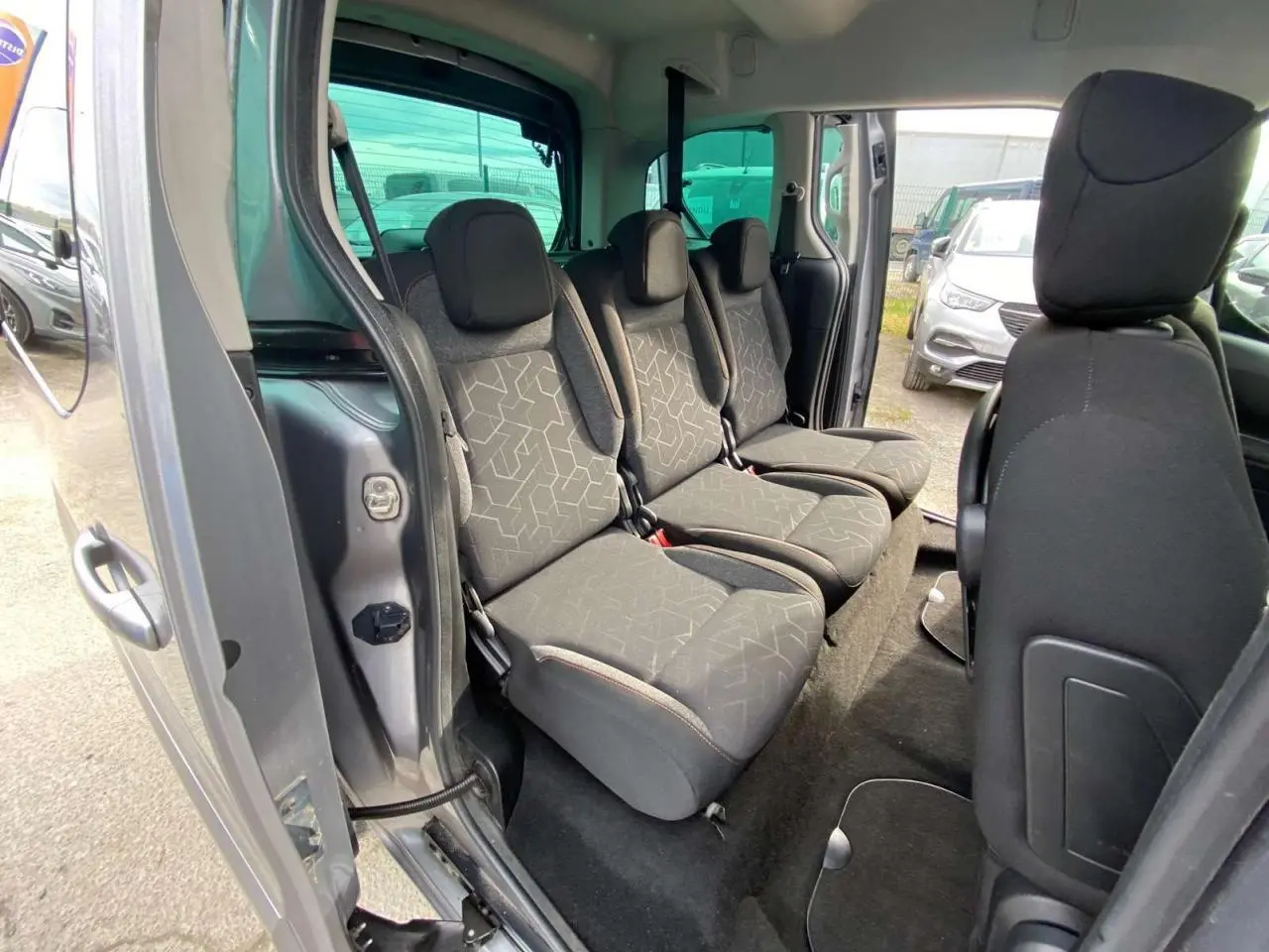 Vue intérieure côté gauche du Peugeot Partner gris Artense, montrant la banquette arrière 2/3-1/3 avec sièges en tissu noir.