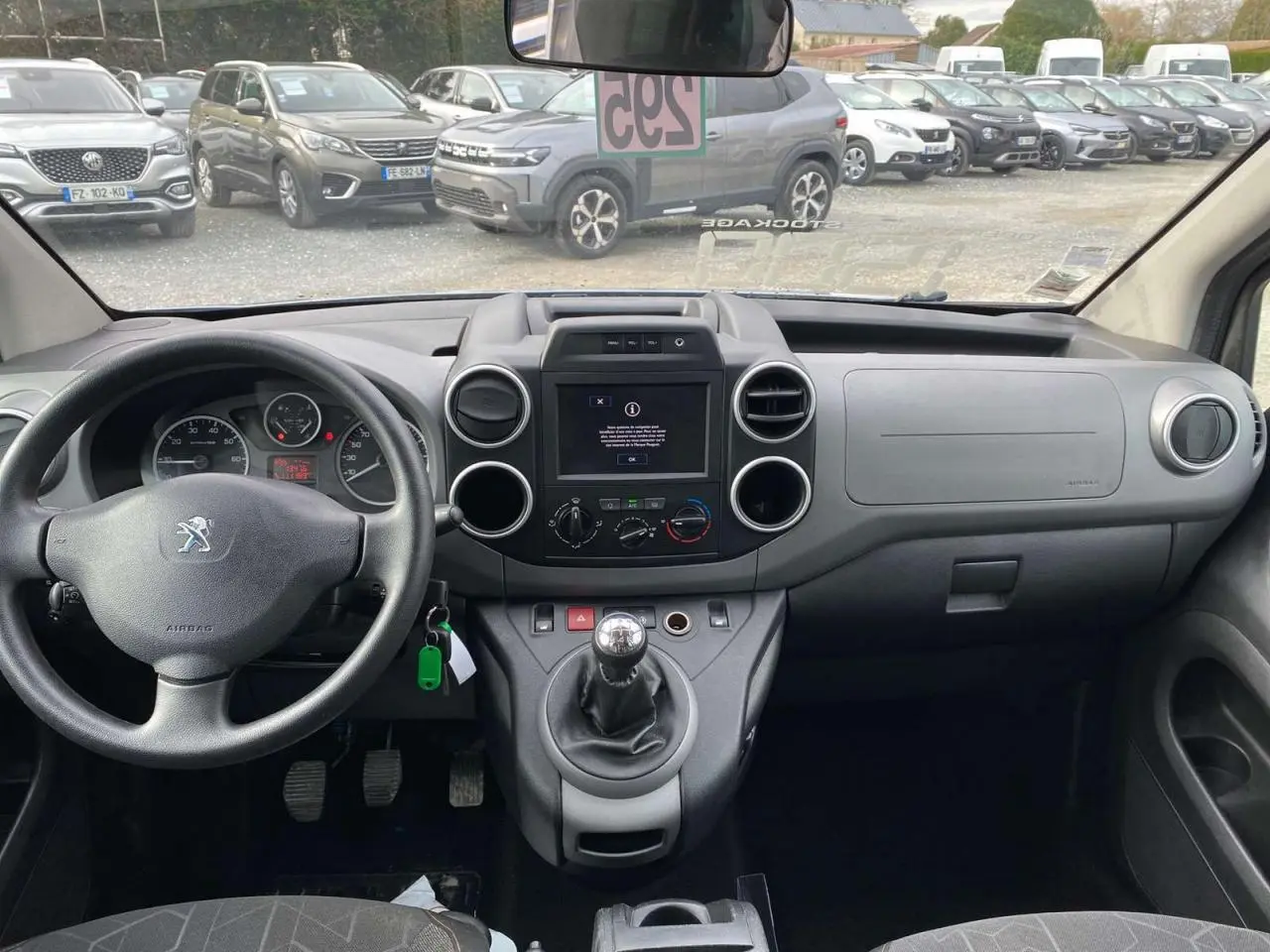 Vue intérieure frontale du tableau de bord du Peugeot Partner gris, avec volant, écran tactile et levier de vitesse manuel.