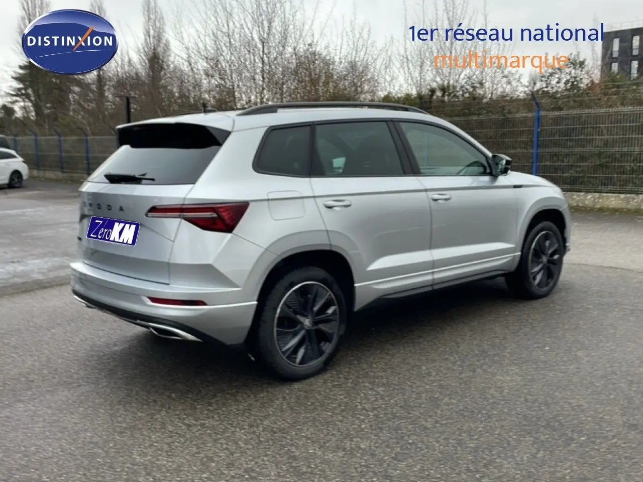 Vue 3/4 arrière droite d’un Skoda Karoq gris argent métal 2025 avec jantes noires et toit ouvrant.